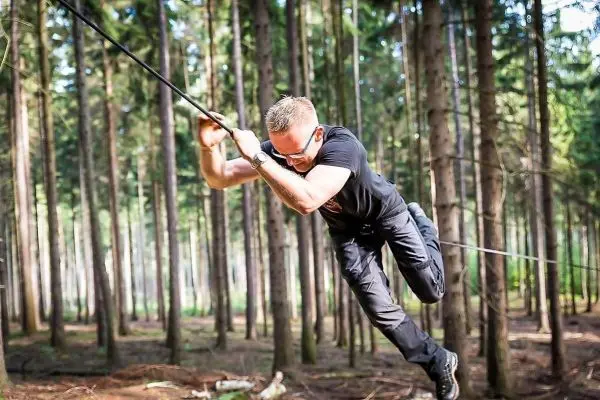 Mann überquert selbstgebaute Seilbrücke zwischen Bäumen im Wald