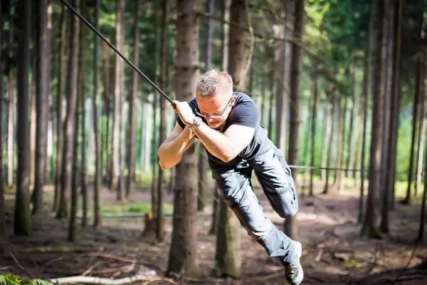 Mann überquert selbstgebaute Seilbrücke zwischen Bäumen im Wald