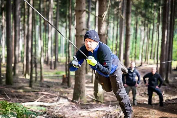 Mann überquert selbstgebaute Seilbrücke zwischen Bäumen im Wald