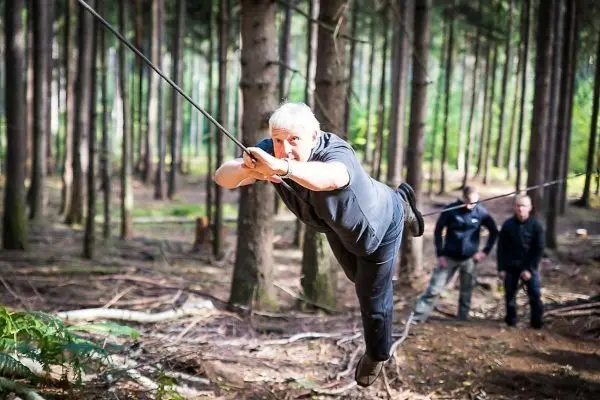 Mann überquert selbstgebaute Seilbrücke zwischen Bäumen im Wald