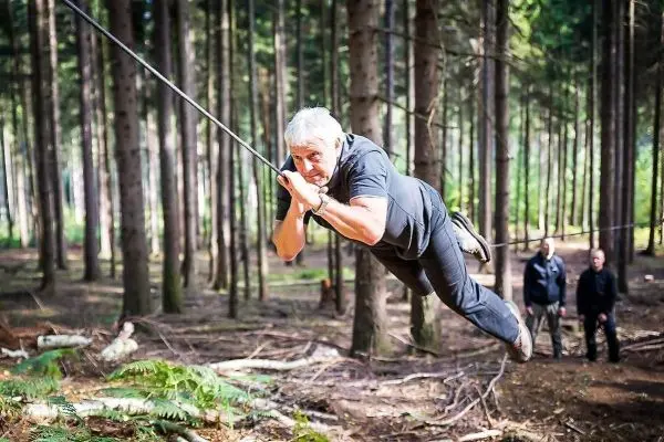 Mann überquert selbstgebaute Seilbrücke zwischen Bäumen im Wald