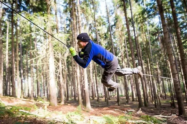 Mann überquert selbstgebaute Seilbrücke zwischen Bäumen im Wald