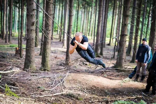 Mann überquert selbstgebaute Seilbrücke zwischen Bäumen im Wald