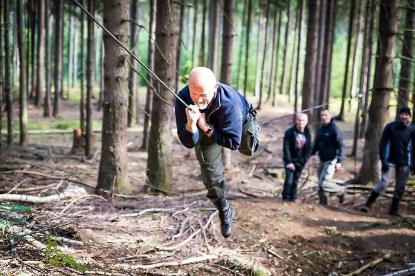 Mann überquert selbstgebaute Seilbrücke zwischen Bäumen im Wald