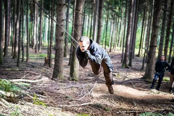 Mann überquert selbstgebaute Seilbrücke zwischen Bäumen im Wald