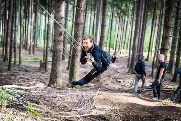 Mann überquert selbstgebaute Seilbrücke zwischen Bäumen im Wald