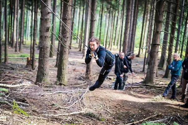 Mann überquert selbstgebaute Seilbrücke zwischen Bäumen im Wald