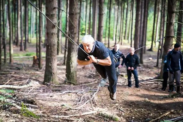 Mann überquert selbstgebaute Seilbrücke zwischen Bäumen im Wald