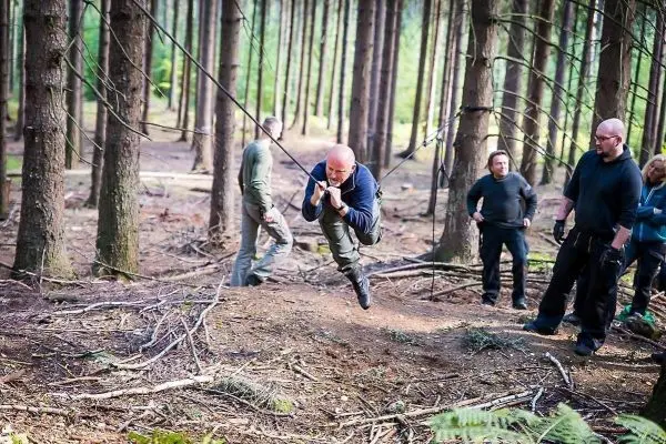 Mann überquert selbstgebaute Seilbrücke zwischen Bäumen im Wald