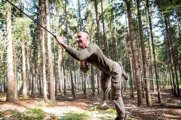 Mann überquert selbstgebaute Seilbrücke zwischen Bäumen im Wald