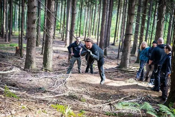 Mann zieht an einem Seil in einem Wald, mehrere Personen beobachten