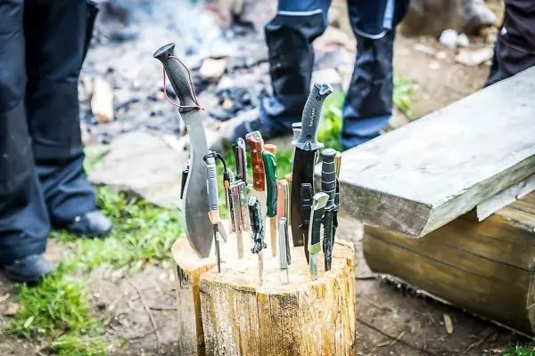 Mehrere Messer stecken in einem Holzblock neben einem Lagerfeuer