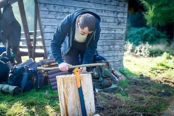 Messer bearbeitet Holzblock auf dem Boden neben einer Holzstruktur