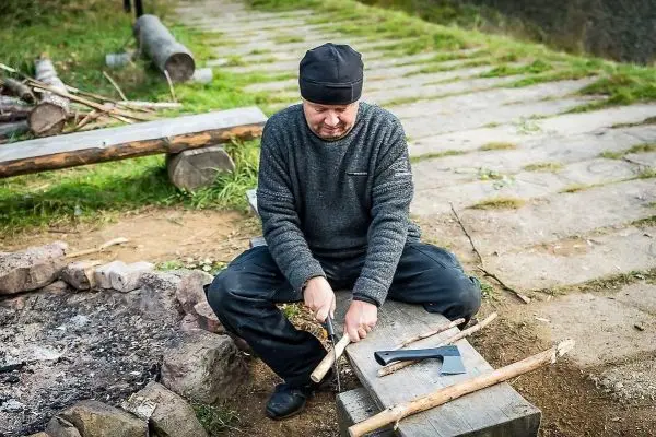 Messer bearbeitet Holzstück auf einer Holzbank neben einem kleinen Feuer