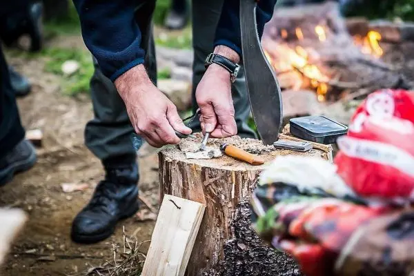 Messer schneidet Zunder auf einem Baumstumpf neben einem kleinen Feuer