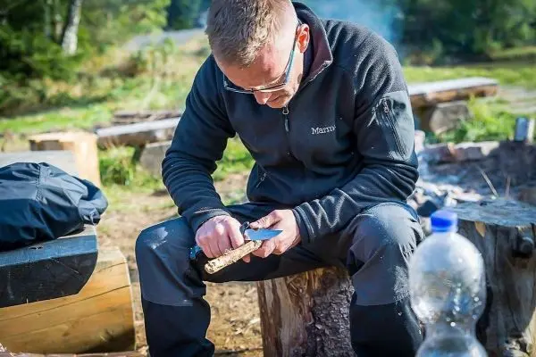 Messer schnitzt in Holzstück während auf Baumstumpf gesessen wird