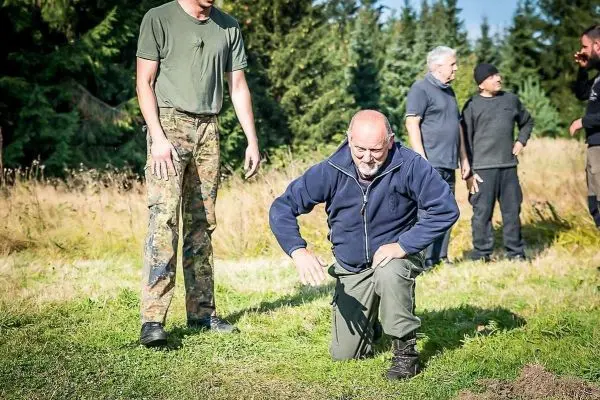 Person kniet auf dem Boden und untersucht den Untergrund beim Überlebenstraining