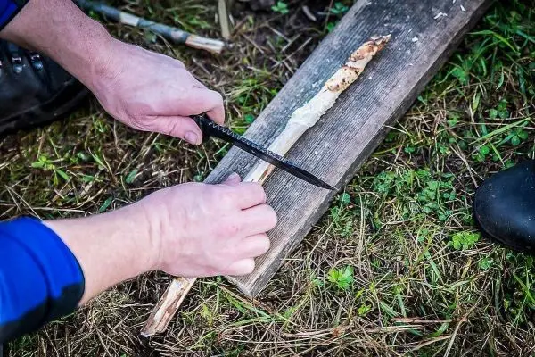 Person schneidet mit einem Messer einen Stock auf einem Brett