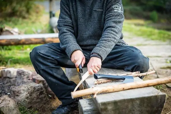 Person schnitzt mit einem Messer einen Stock auf einem Holzblock