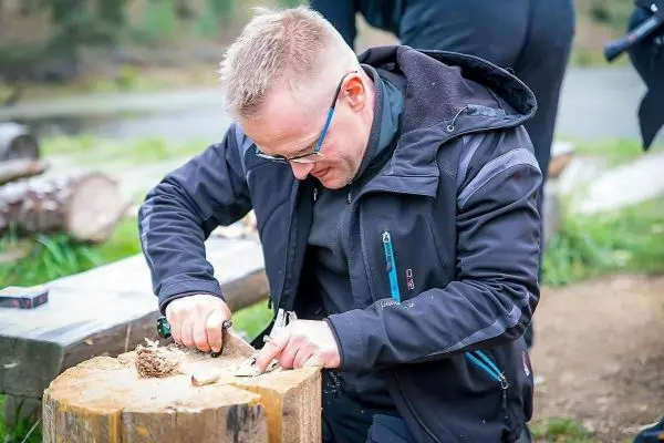 Person schnitzt mit einem Messer in einen Holzblock beim Überlebenstraining