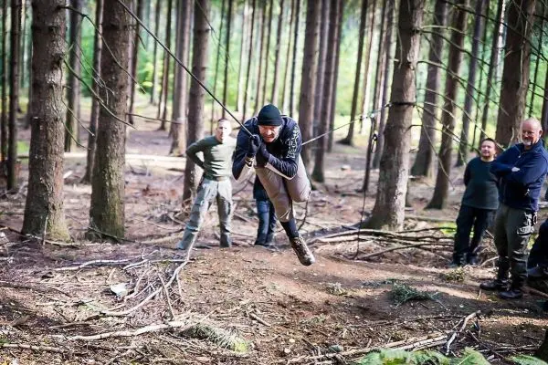 Person schwingt an Seil zwischen Bäumen, andere Personen beobachten