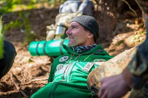 Person sitzt am Boden und lächelt im Wald beim Überlebenstraining