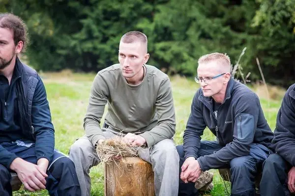 Person sitzt auf einem Holzblock und hält Gras in der Hand