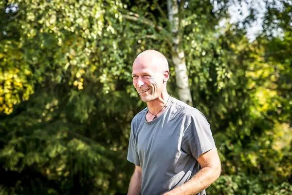 Person steht lächelnd im Freien zwischen Bäumen
