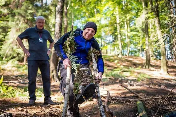 Person trägt selbstgebaute Trage aus Ästen und Pflanzenmaterial im Wald