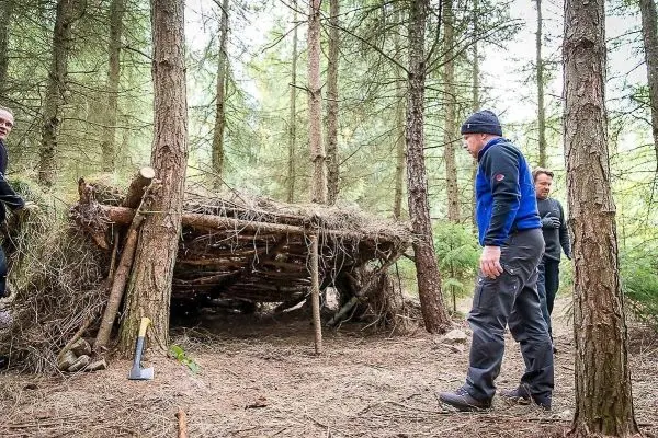 Personen betrachten eine selbstgebaute Unterkunft im Wald