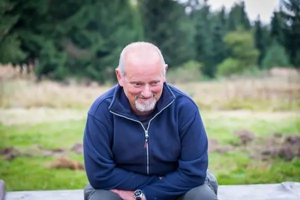 Sitzende Person mit kurzem Haar und Bart auf einer Holzbank im Freien