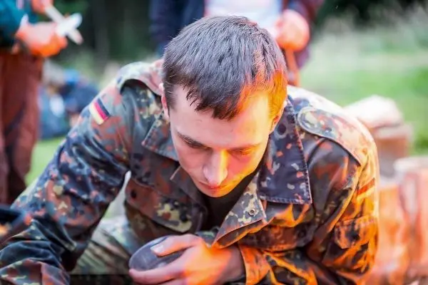 Soldat in Tarnuniform bearbeitet einen Gegenstand in der Nähe eines Feuers