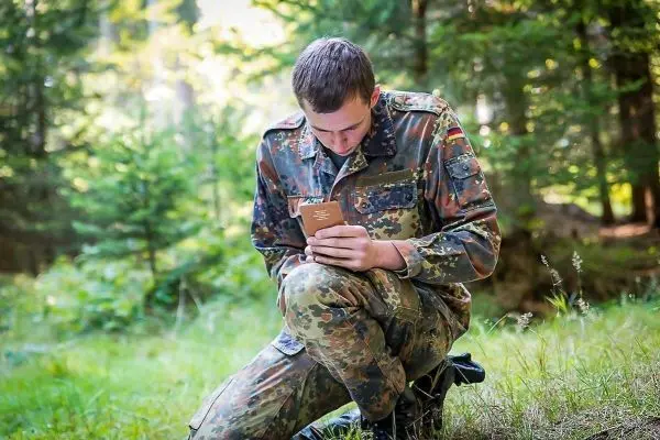 Soldat kniet im Wald und liest in einem Notizbuch