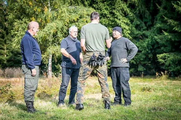 Vier Personen stehen im Gespräch in einer Waldlichtung