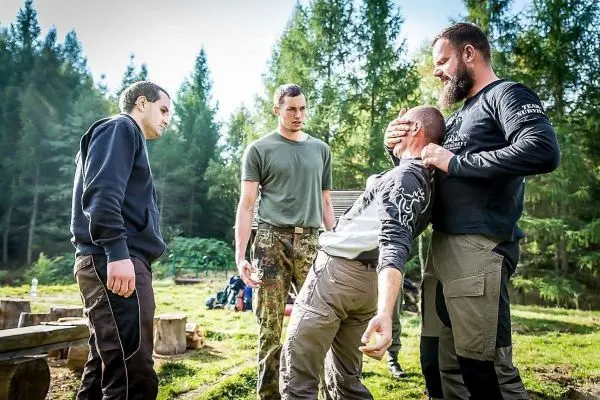 Vier Personen üben eine Technik zur Selbstverteidigung im Wald