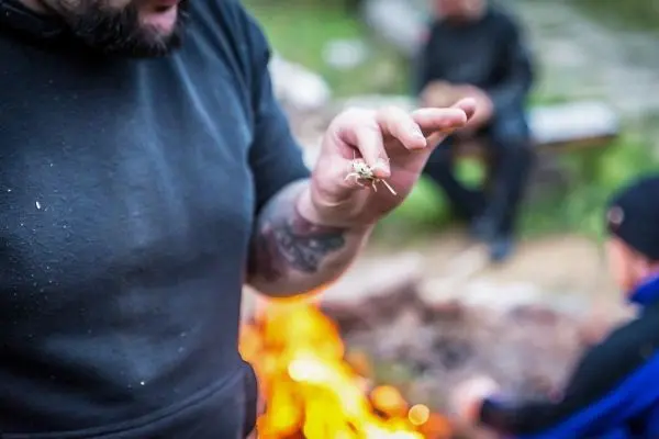 Zunder wird in der Hand gehalten, während ein Feuer im Hintergrund brennt