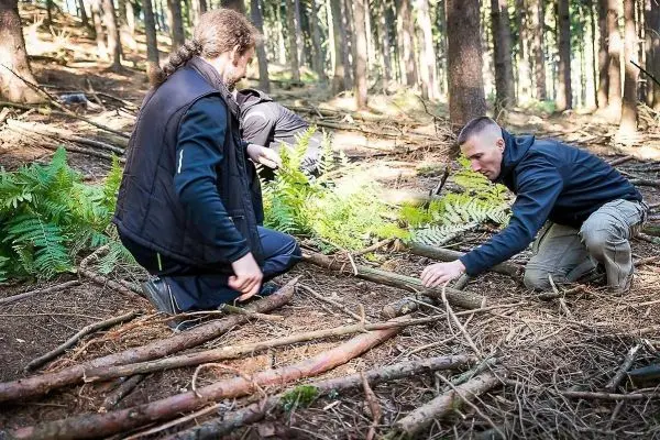 Zwei Personen bauen eine Konstruktion aus Ästen im Wald