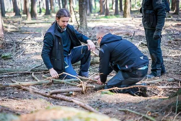Zwei Personen bauen eine selbstgebaute Konstruktion aus Ästen im Wald