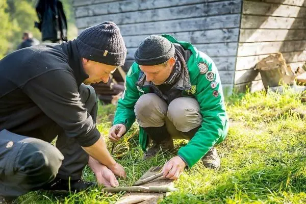 Zwei Personen bearbeiten Holzstücke auf dem Boden in einer Wiese