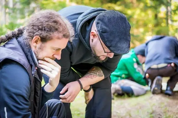 Zwei Personen beugen sich über den Boden und betrachten etwas aufmerksam