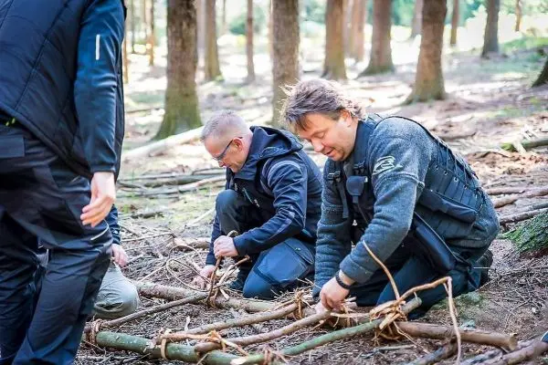 Zwei Personen binden Äste mit Schnur im Wald zusammen