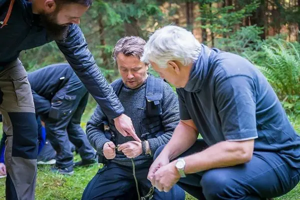 Zwei Personen knien im Wald und arbeiten an einem Seil