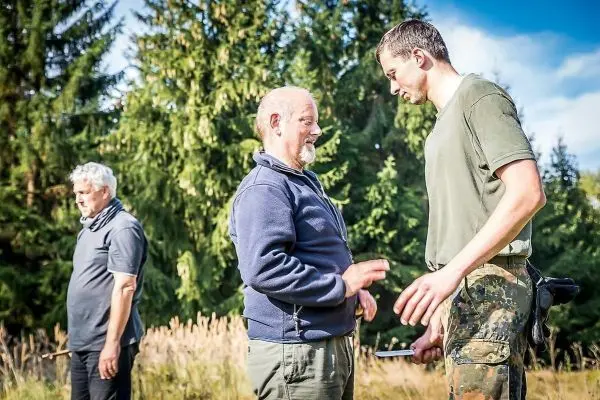 Zwei Personen stehen im Gespräch, eine dritte Person im Hintergrund beobachtet