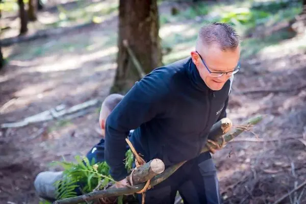 Zwei Personen tragen einen Holzstamm durch den Wald