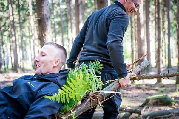 Zwei Personen transportieren improvisierte Trage aus Ästen im Wald