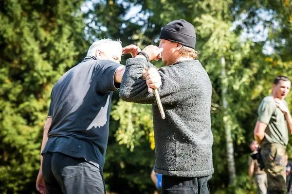 Zwei Personen üben eine Nahkampftechnik mit einem Stock im Freien