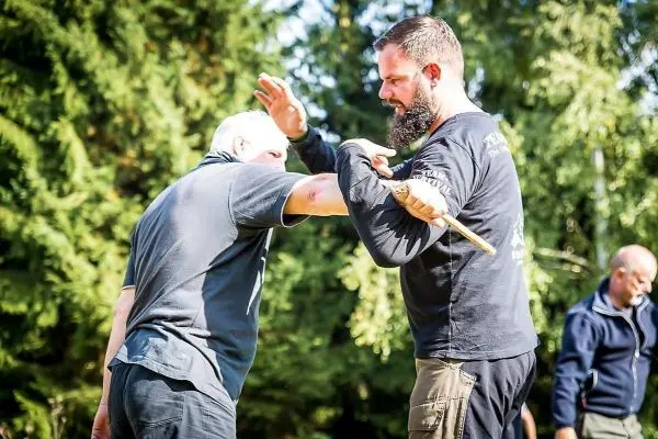 Zwei Personen üben eine Selbstverteidigungstechnik mit einem Stock im Freien