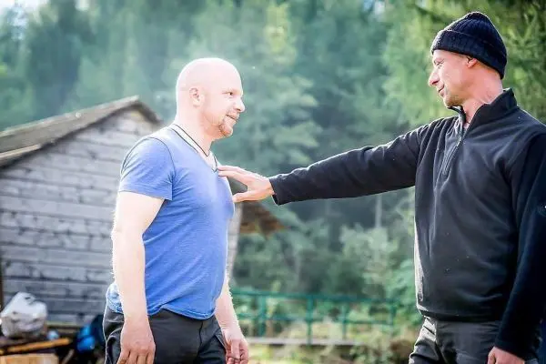 Zwei Personen üben eine Technik im Freien, eine Holzstruktur im Hintergrund