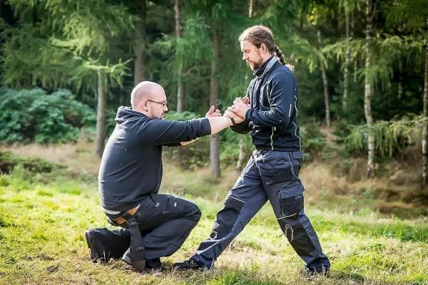 Zwei Personen üben eine Technik im Freien, einer kniet und greift den anderen