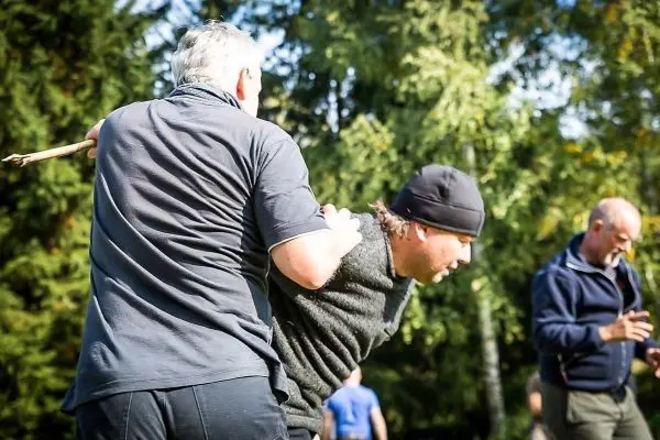 Zwei Personen üben eine Technik zur Kontrolle mit einem Stock im Freien